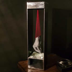 The nightlight is a tabletop light featuring a cast aluminum hand suspended with red floss over an illuminated landscape