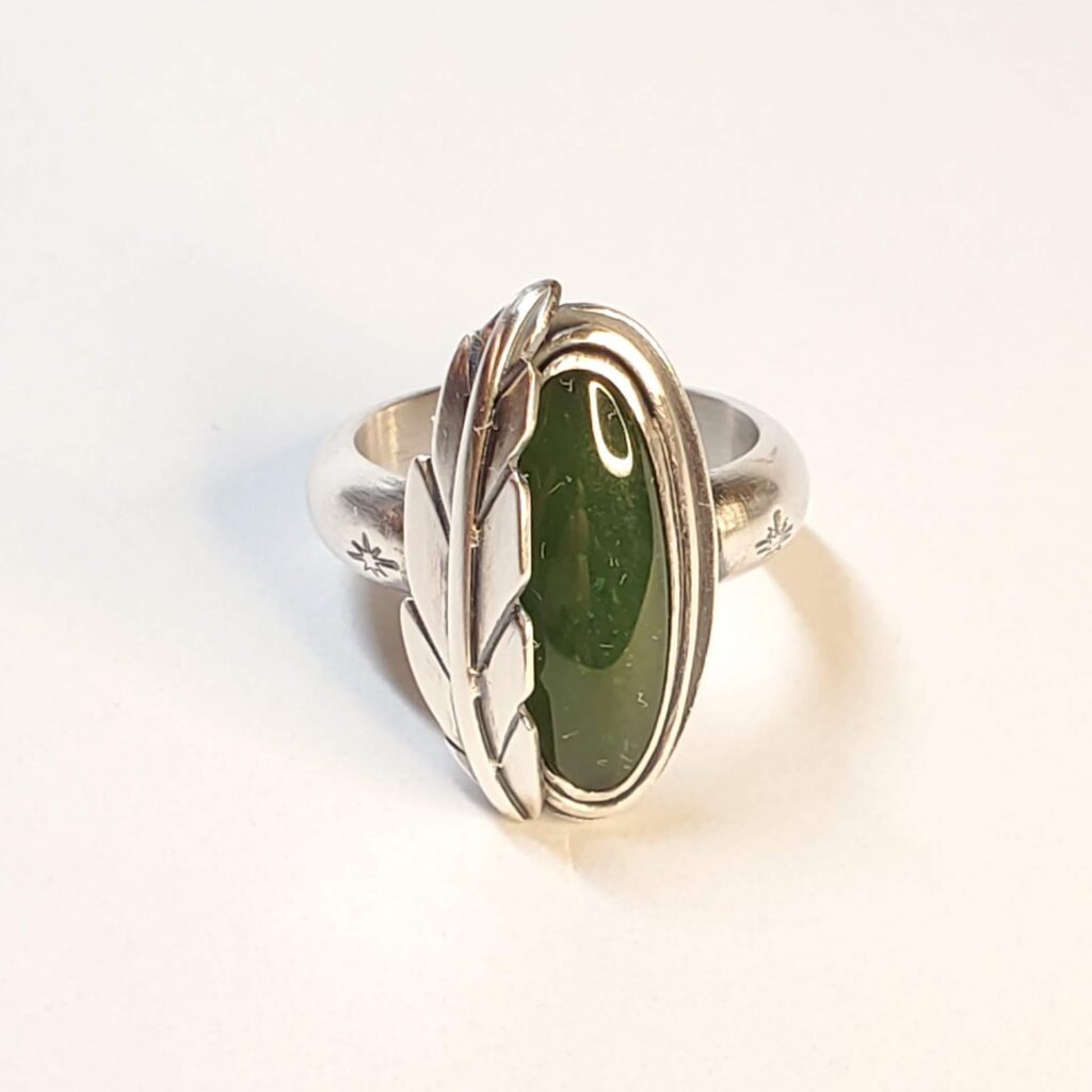 A sterling silver ring set with an oval, green jade. Hugging the left side of the stone is a formed silver feather made in the Southwest style.