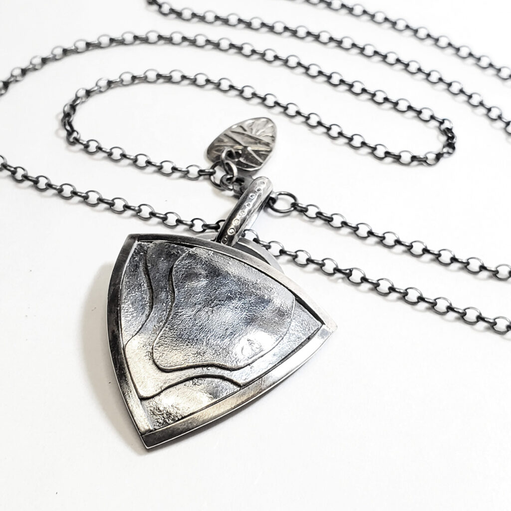 Another closeup of the trillion-shaped pendant with its silver rollo chain, taken from a different perspective .