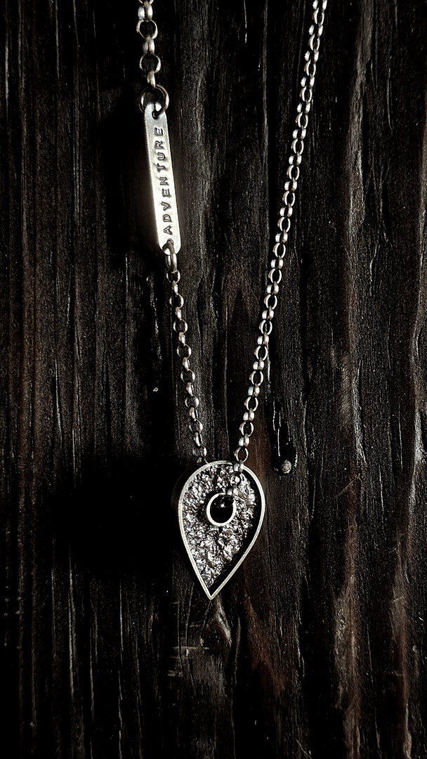 A necklace featuring a map marker planchette pendant made with reticulated silver and framed in a narrow sterling silver strip