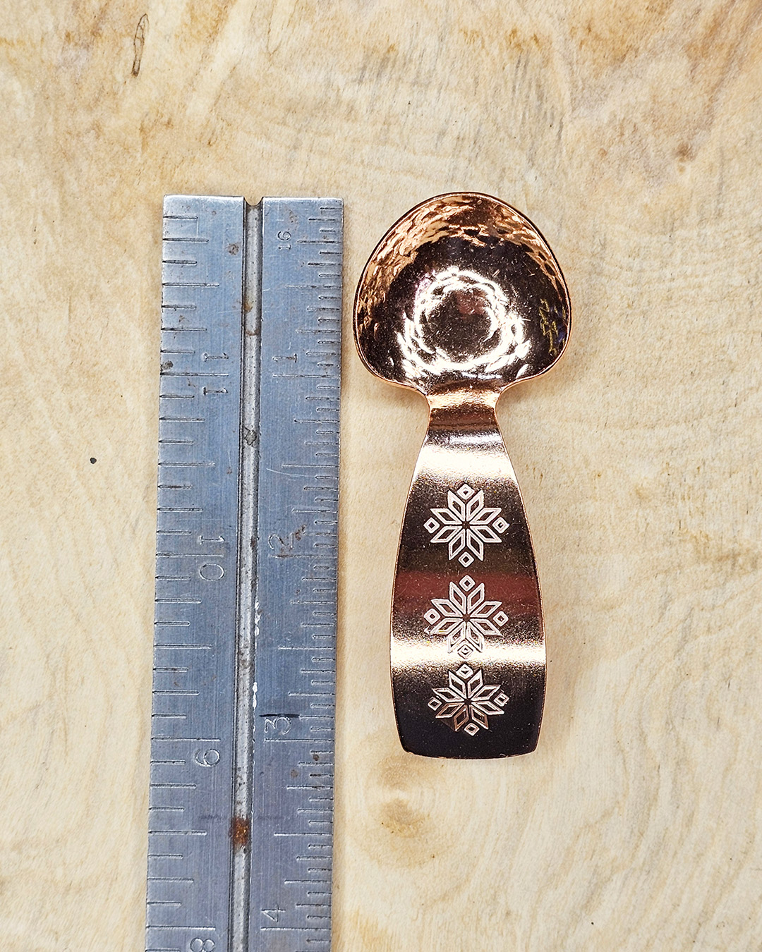 A small copper spoon stamped with three traditional eight-pointed stars, measured next to a ruler