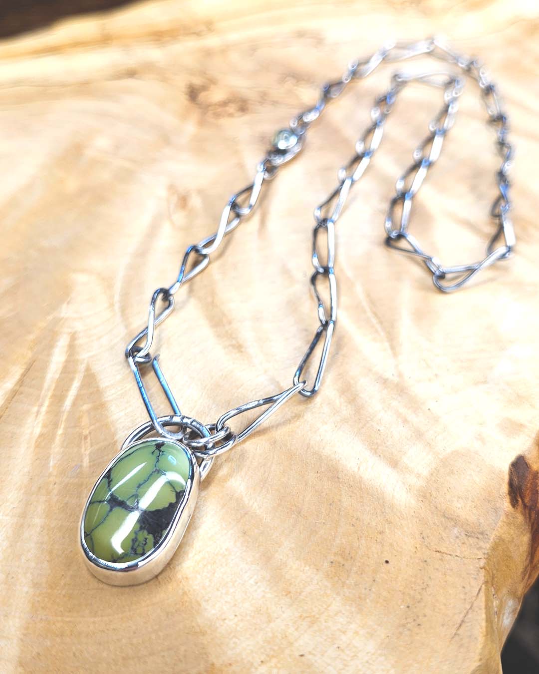 A green turquoise pendant on a handmade silver chain. A Prehenite cabochon is set in the chain to accent the green of the turquoise
