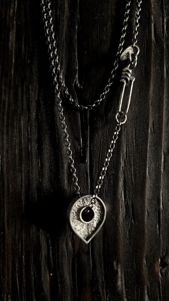 A necklace featuring a map marker planchette pendant made with reticulated silver and framed in a narrow sterling silver strip
