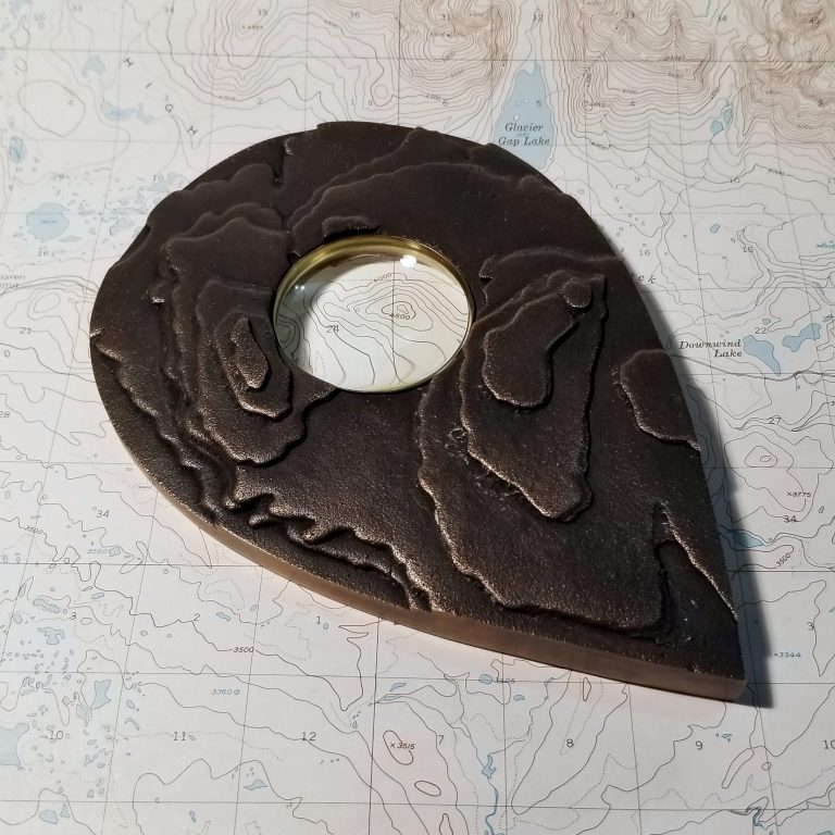 An overhead photo of a bronze map marker set with a reclaimed glass lens