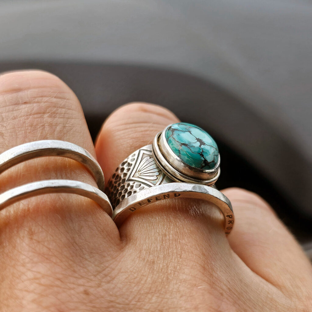 A stamped turquoise ring worn on the right hand, and accompanied by a thin silver band
