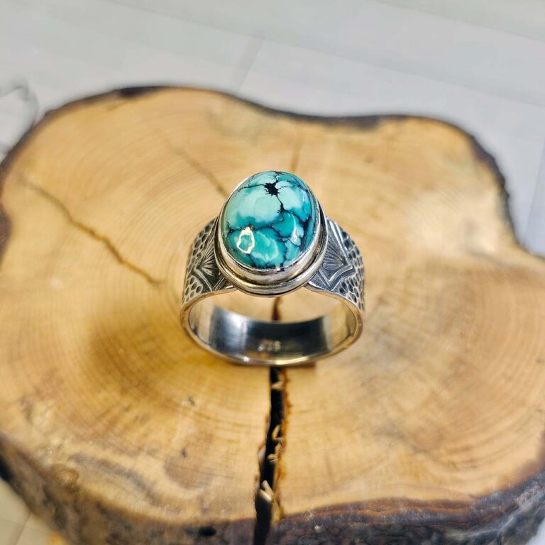 A stamped turquoise ring sitting on a small cross-section of wood.
