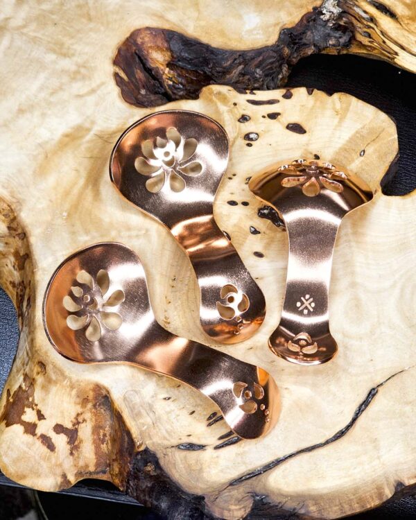 Three copper condiment spoons on a wood surface