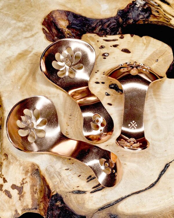 Three copper condiment spoons on a wood surface