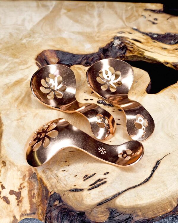 Three copper condiment spoons on a wood surface