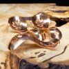 Three copper condiment spoons on a wood surface