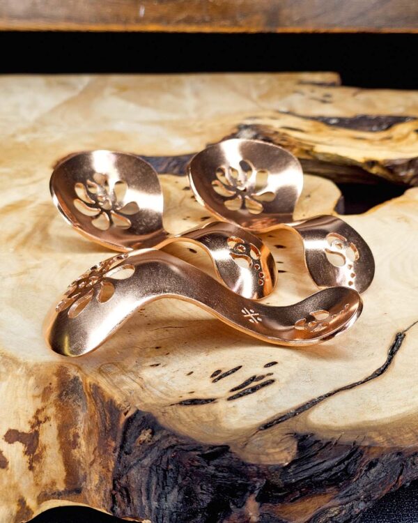 Three copper condiment spoons on a wood surface