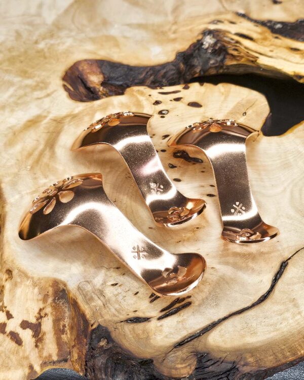 Three copper condiment spoons on a wood surface