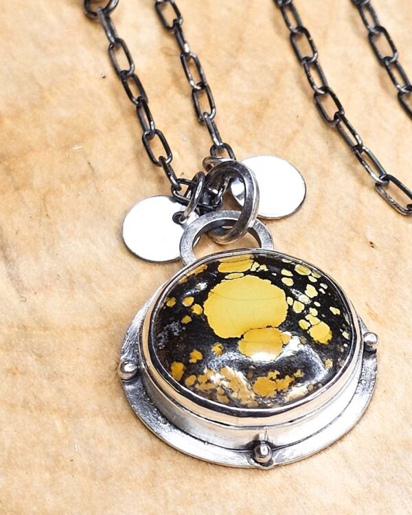 A pendant set with a yellow turquoise on a sterling silver chain sits on a wood background