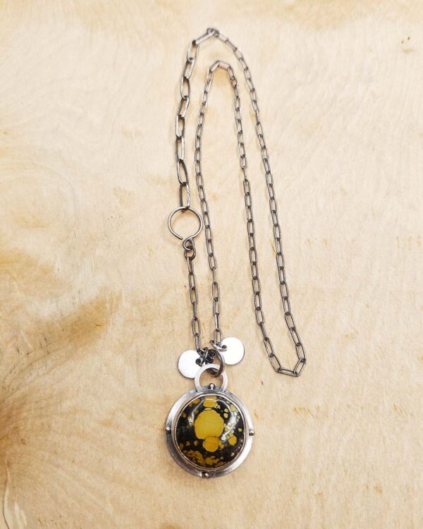 A pendant set with a yellow turquoise on a sterling silver chain sits on a wood background
