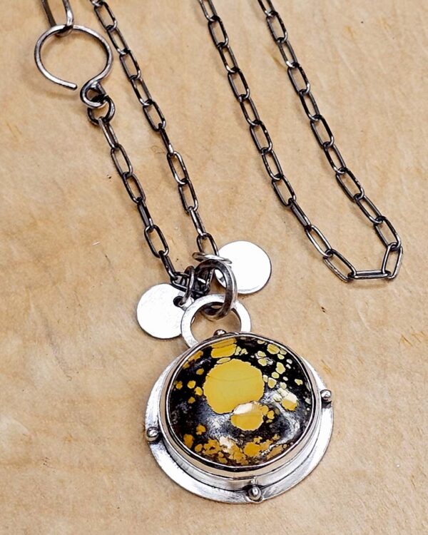 A pendant set with a yellow turquoise on a sterling silver chain sits on a wood background